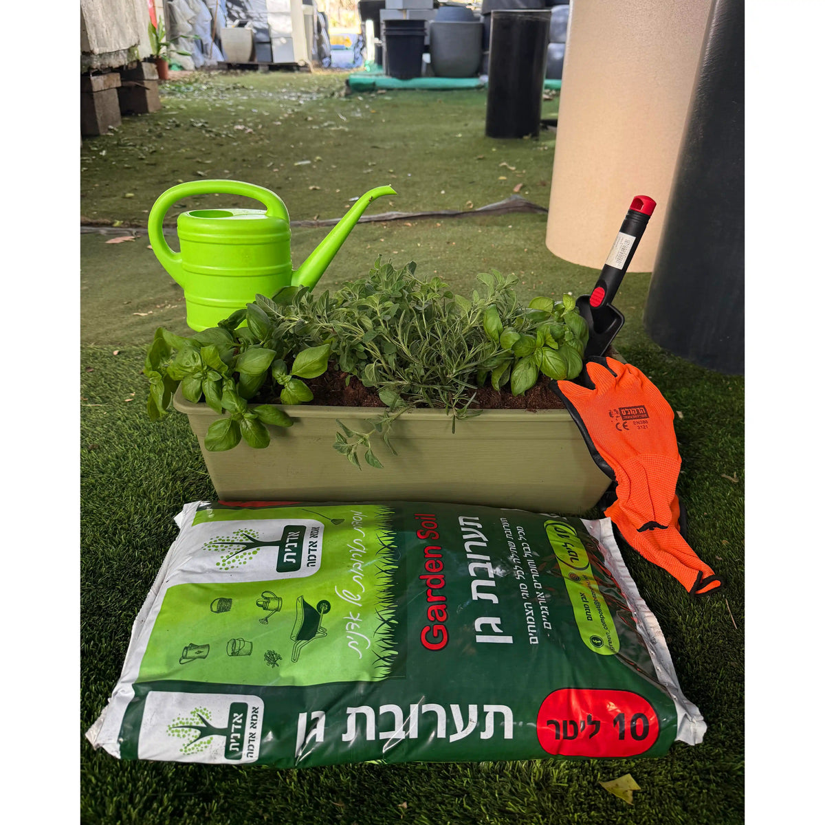 ציוד גינון הכולל משפך ירוק , צמחים בתוך אדנית ירוקה כהה, כפפות ושק אדמה, מונחים על דשא.